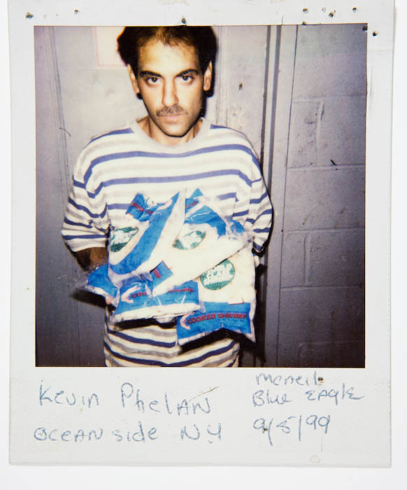 Man in a blue and white striped shirt holding an armful of bagged frozen cooked shrimp.