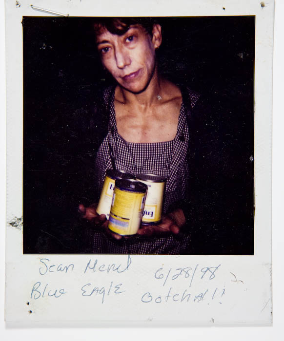 Woman in a checked dress holding three cans of Enfamil infant formula.