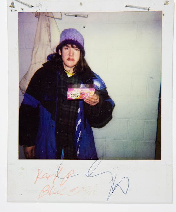 Young man in a purple knit hat and layered winter coats holding out a box of Good and Fruity candy.