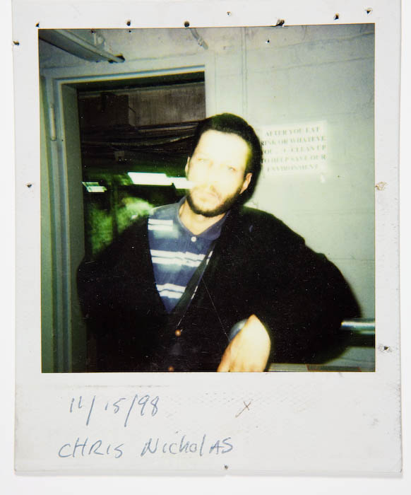 Motion-blurred photo of a bearded man in a striped shirt and dark jacket standing in a stockroom doorway.