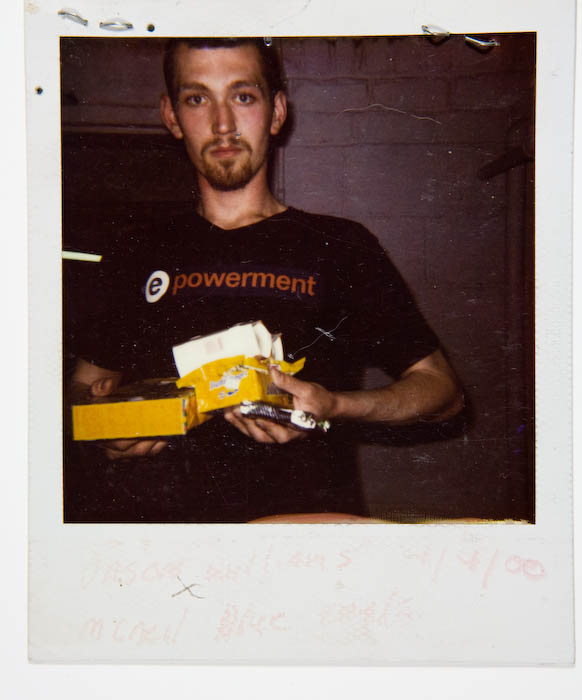 Young man in a black epowerment T-shirt holding an opened yellow carton of cigarettes.