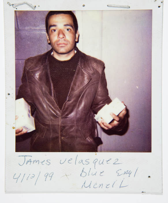 Man in a brown leather jacket holding out a small white boxed item in each hand.
