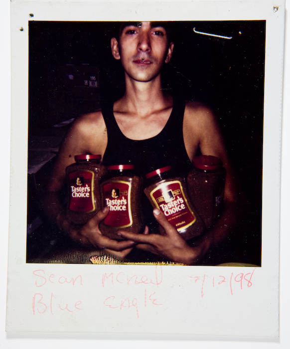 Young man in a black tank top holding an armful of Taster's Choice instant coffee jars.