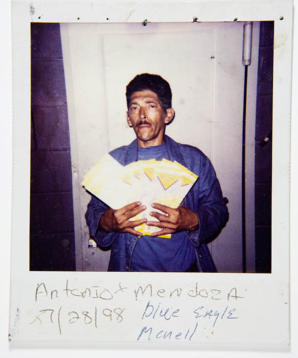 Man in blue work coveralls fanning out a spread of yellow and white packets in both hands.