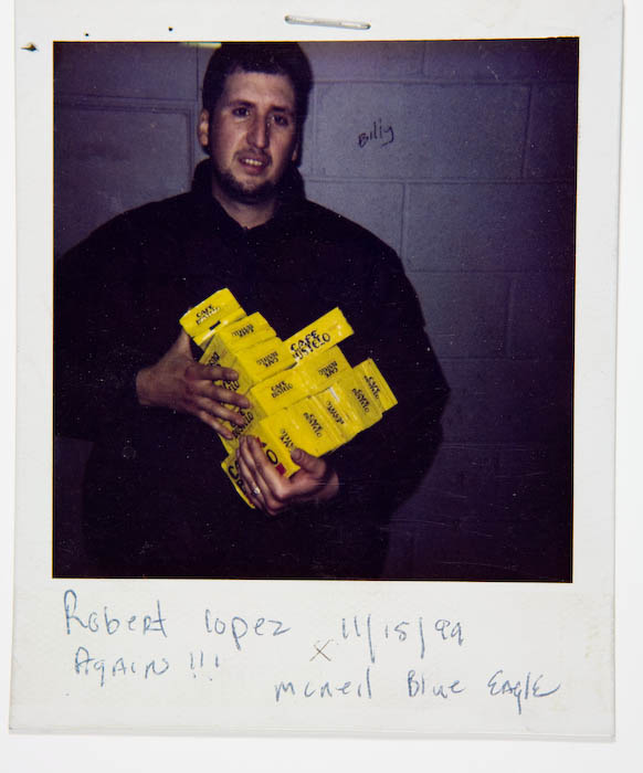 Man in a black jacket holding an armful of yellow bricks of Cafe Bustelo coffee.